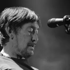 Chris Rea, zamyślony, przed mikrofonem na scenie.