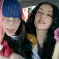 Dwie młode kobiety, jedna z nich przypomina brata Billie Eilish, trzymają w rękach kolorowe tkaniny, bawiąc się w samochodzie.