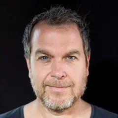 Marcel Woods, z niebieskimi oczami i siwiejącą brodą, patrzy prosto w obiektyw.