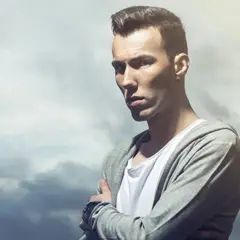 Młody mężczyzna w bluzie z kapturem, jeden z znani polscy dj, z rękami skrzyżowanymi na piersi.