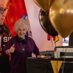 Uśmiechnięta starsza pani z słuchawkami na szyi, dająca kciuk w górę przy stanowisku DJ-a. To DJ Rush w akcji!