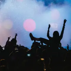 Tłumy na płock festiwal bawią się pod sceną. Jedna osoba niesiona jest na rękach, z ramionami uniesionymi w górę.