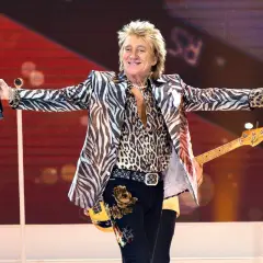 Rod Stewart w panterce i marynarce w zebrę, z gitarą basową, na scenie, jakby to był największy koncert na świecie.