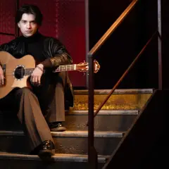 Marcin Patrzałek na koncercie, siedząc na schodach z gitarą, gotowy do występu.