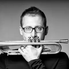 Maciej Fortuna, muzyk z trąbką, w okularach, zamyślony.