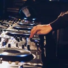 Ręka DJ-a miksuje utwory techno na konsoli.