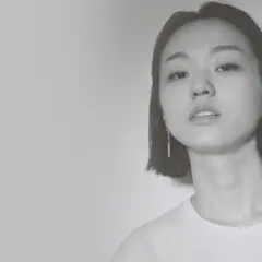 Park Hye Jin, młoda kobieta o krótkich włosach i delikatnym spojrzeniu, w białej koszulce i długich kolczykach.