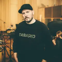 W studiu nagraniowym, w otoczeniu muzyków, stoi jeden z legend polskiego rapu, w bluzie z napisem "TABASKO".