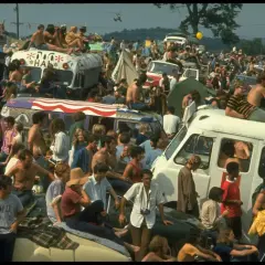 Tłum ludzi na festiwalu, siedzący na dachach vanów i samochodów. To właśnie woodstock co to za wydarzenie?
