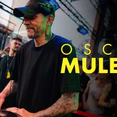 Oscar Mulero, DJ z tatuażami, miksuje muzykę na żywo, podczas gdy tłum ludzi bawi się w tle. Arte.