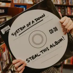 Ręce trzymają okładkę płyty System of a Down "Steal This Album!". Wybór między winyl czy CD jest tu oczywisty.