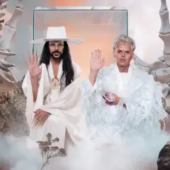 Dwóch mężczyzn w białych strojach, otoczonych kośćmi i mgłą, jakby w surrealistycznym imperium słońca.
