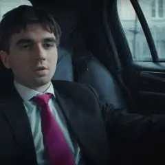 Młody mężczyzna w garniturze i fuksjowym krawacie siedzi w samochodzie. Czy mata jest w SBM?