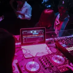 DJ Glasse miksuje muzykę na imprezie. Laptop i sprzęt DJ-ski w różowym świetle.