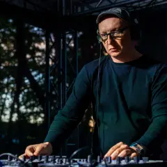 Mr Lex w okularach i czapce, w słuchawkach, miksuje muzykę na konsoli DJ-skiej.