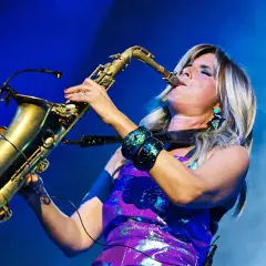 Candy Dulfer gra na saksofonie, jej blond włosy opadają na fioletową, błyszczącą sukienkę.
