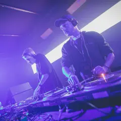 Dwóch techno djs w słuchawkach miksuje muzykę na żywo, tworząc energetyczną atmosferę na scenie.