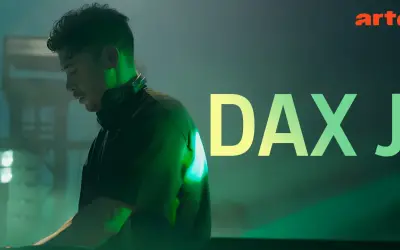 Dax J, DJ w słuchawkach, w zielonym świetle, z napisem "DAX J" i logo Arte.