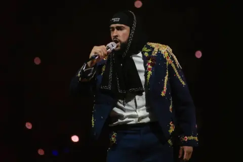 Bad Bunny w Polsce, w ozdobnej marynarce i czapce z napisem "Puerto Rico", śpiewa do mikrofonu na tle rozmytych świateł.
