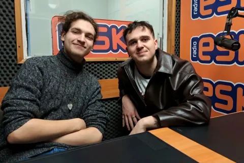 Dwóch młodych mężczyzn w studiu radiowym. Jeden w swetrze, drugi w skórzanej kurtce. Może to jeżyk raper i jego kolega?