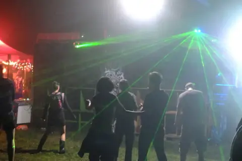 Nocna impreza z laserami, ludzie tańczą w rytm techno. Wykonawcy z lat 2000 tworzą niezapomnianą atmosferę.