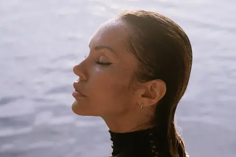 Deborah de Luca z zamkniętymi oczami, w profilu, na tle wody.