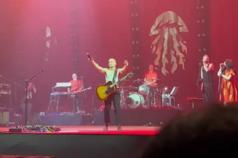 Krzysztof Zalewski koncert: wokalista z gitarą na scenie, zespół gra, tłum szaleje.