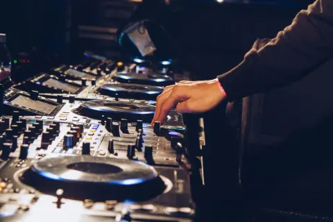 Ręka DJ-a miksuje utwory techno na konsoli.