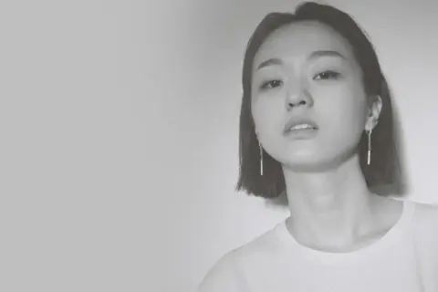 Park Hye Jin, młoda kobieta o krótkich włosach i delikatnym spojrzeniu, w białej koszulce i długich kolczykach.