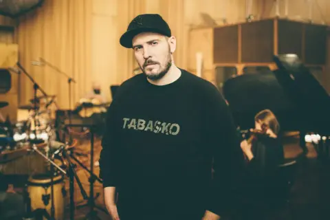 W studiu nagraniowym, w otoczeniu muzyków, stoi jeden z legend polskiego rapu, w bluzie z napisem "TABASKO".