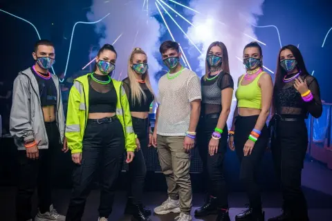 Grupa młodych ludzi w maskach i neonowych akcesoriach, gotowa na energetyczny koncert techno.