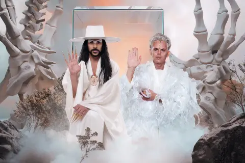 Dwóch mężczyzn w białych strojach, otoczonych kośćmi i mgłą, jakby w surrealistycznym imperium słońca.