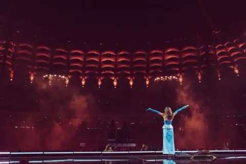 Sanah w błękitnej sukni na tle sceny z czerwonymi światłami. Już wkrótce kolejne sanah koncerty 2026!