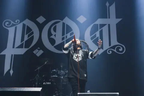 Sonny Sandoval z P.O.D. śpiewa na scenie, z charakterystycznym logo zespołu w tle.