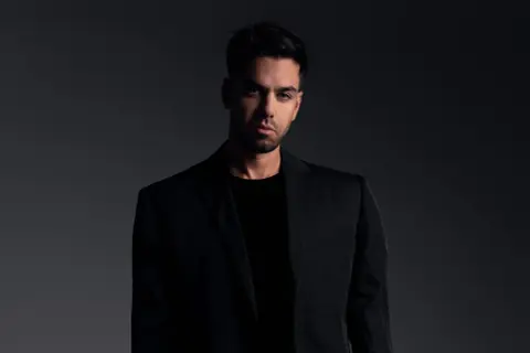 Matteo Milleri w czarnym garniturze, zamyślony, patrzy prosto w obiektyw.