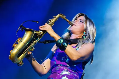 Candy Dulfer gra na saksofonie, jej blond włosy opadają na fioletową, błyszczącą sukienkę.