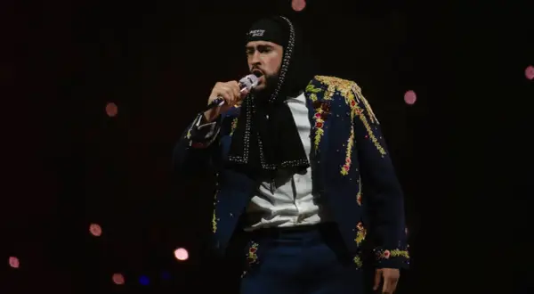 Bad Bunny w Polsce, w ozdobnej marynarce i czapce z napisem "Puerto Rico", śpiewa do mikrofonu na tle rozmytych świateł.