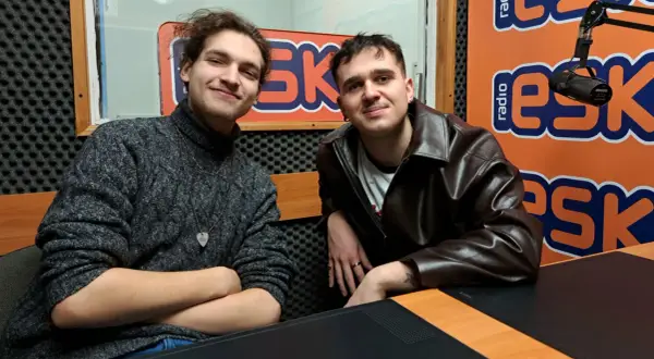 Dwóch młodych mężczyzn w studiu radiowym. Jeden w swetrze, drugi w skórzanej kurtce. Może to jeżyk raper i jego kolega?