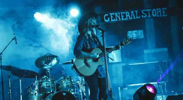 Gwiazdy country w kowbojskich kapeluszach grają na gitarach i śpiewają na scenie, otoczone dymem i niebieskim światłem.