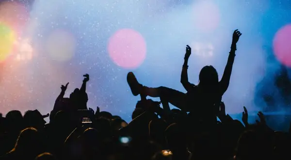 Tłumy na płock festiwal bawią się pod sceną. Jedna osoba niesiona jest na rękach, z ramionami uniesionymi w górę.