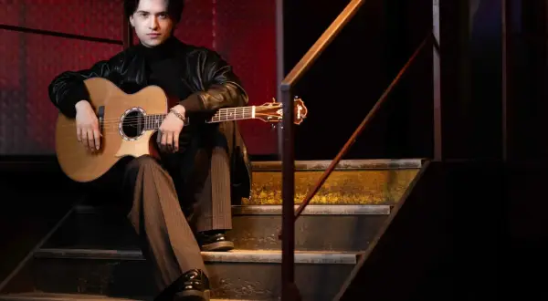 Marcin Patrzałek na koncercie, siedząc na schodach z gitarą, gotowy do występu.
