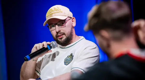 Raper Edzio w bejsbolówce Von Dutch i okularach, trzymający mikrofon, podczas panelu dyskusyjnego.
