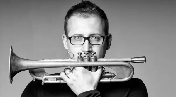 Maciej Fortuna, muzyk z trąbką, w okularach, zamyślony.
