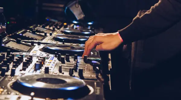 Ręka DJ-a miksuje utwory techno na konsoli.
