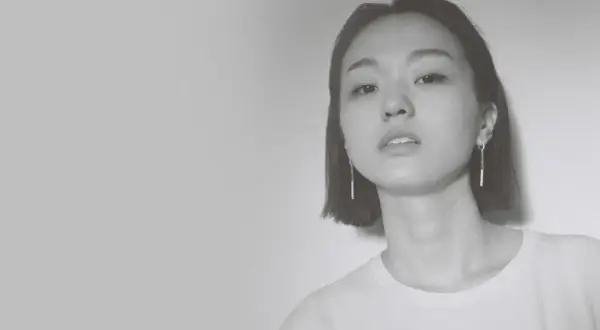 Park Hye Jin, młoda kobieta o krótkich włosach i delikatnym spojrzeniu, w białej koszulce i długich kolczykach.