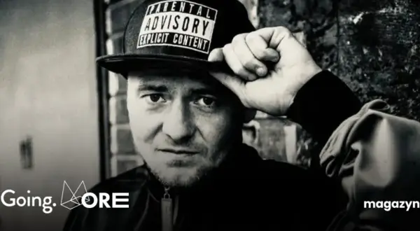 Mężczyzna w czapce z napisem "Parental Advisory Explicit Content" poprawia ją ręką. Jego spojrzenie jest intensywne, jakby mówił: "joka kaliber".