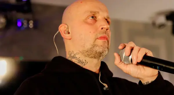 Peja z mikrofonem, w tle światła sceniczne. DJ decki czekają na jego wejście.