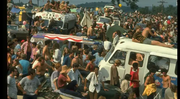 Tłum ludzi na festiwalu, siedzący na dachach vanów i samochodów. To właśnie woodstock co to za wydarzenie?