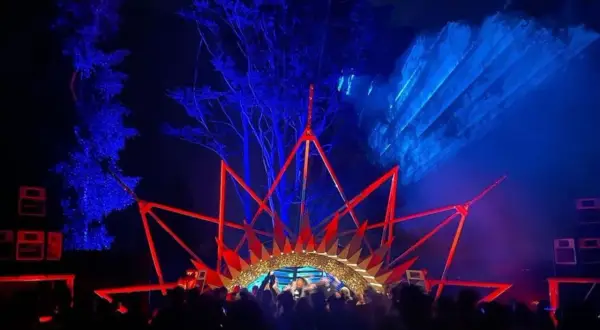 Nocny rave festival z laserami i sceną w kształcie korony. Tłum bawi się w rytm muzyki.