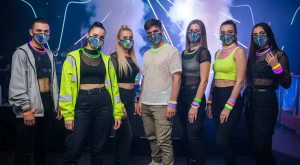 Grupa młodych ludzi w maskach i neonowych akcesoriach, gotowa na energetyczny koncert techno.